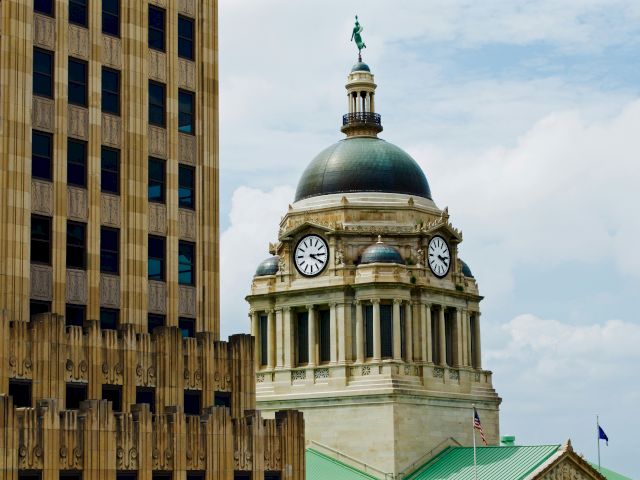 The image shows a historic courthouse dome with a clock, beside a tall building, under a blue sky with clouds.