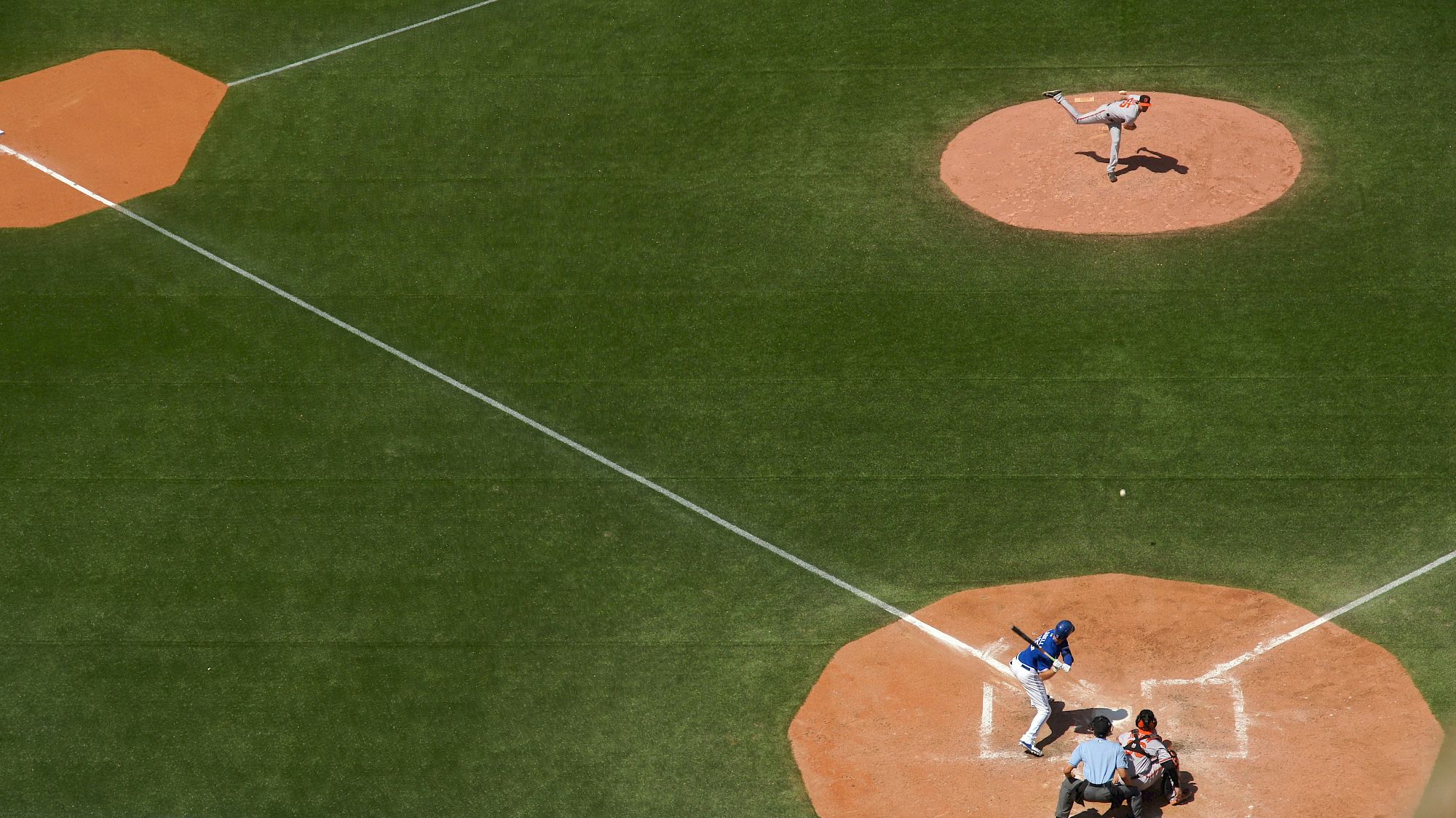 Aerial view of a baseball game showing the pitcher throwing towards the batter, with the umpire and catcher in position.