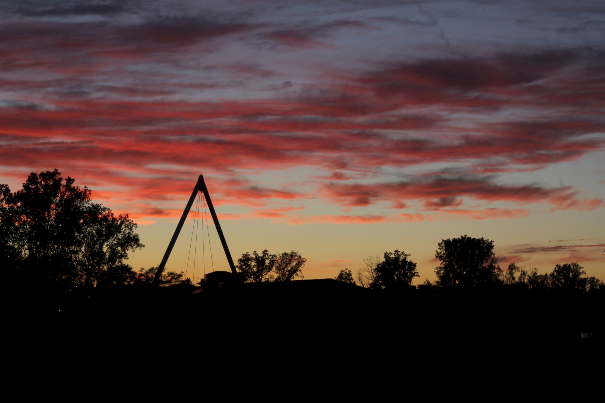 A silhouette of trees and a triangular structure under a vibrant sunset sky with pink and orange clouds is visible.